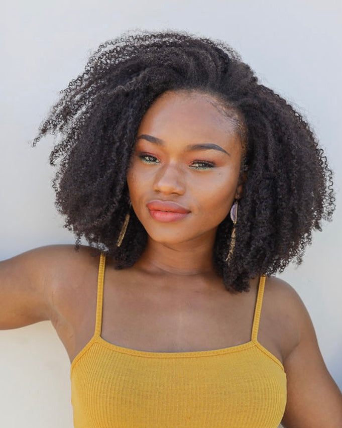 Woman with curly hair wearing a yellow tank top against a white background